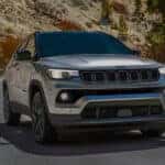 Silver Jeep Compass driving on a winding mountain road with LED headlights illuminated and rocky hillsides in the background.