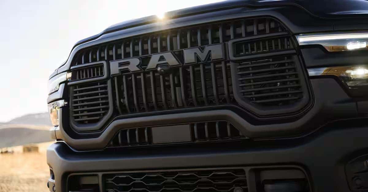 Front close-up of the 2026 Ram 2500 Lunar Edition grille with bold RAM lettering, black grille accents, LED headlights, and sunlight in the background.