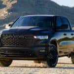 Black 2026 Ram 1500 pickup truck parked on a desert road with rugged mountains in the background under clear daylight.