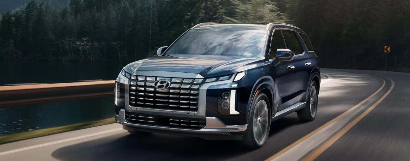 A blue 2025 Hyundai Palisade is shown driving near a lake.
