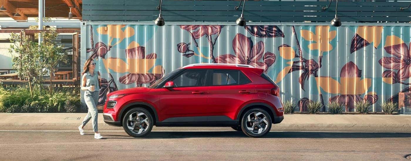 Side view of a red 2023 Hyundai Venue Limited parked in front of a colorful mural.