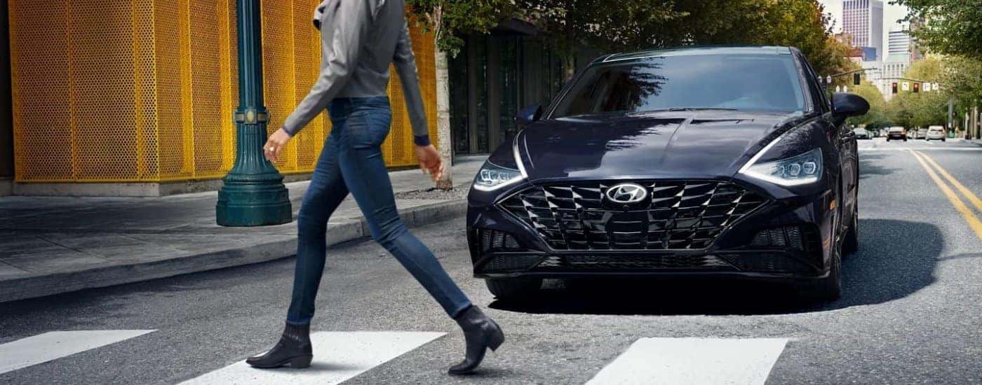A black 2023 Hyundai Sonata is stopped at a crosswalk in a city.