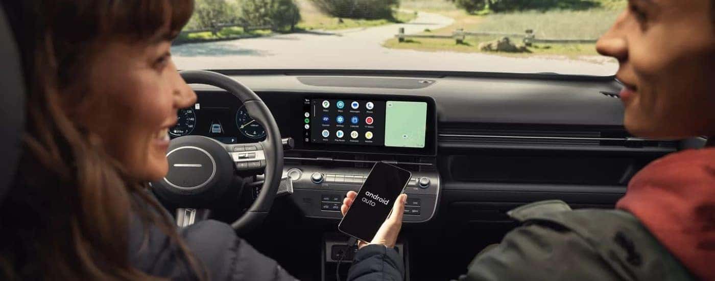A woman and a man are parked in a used 2024 Hyundai Kona for sale on a test drive.