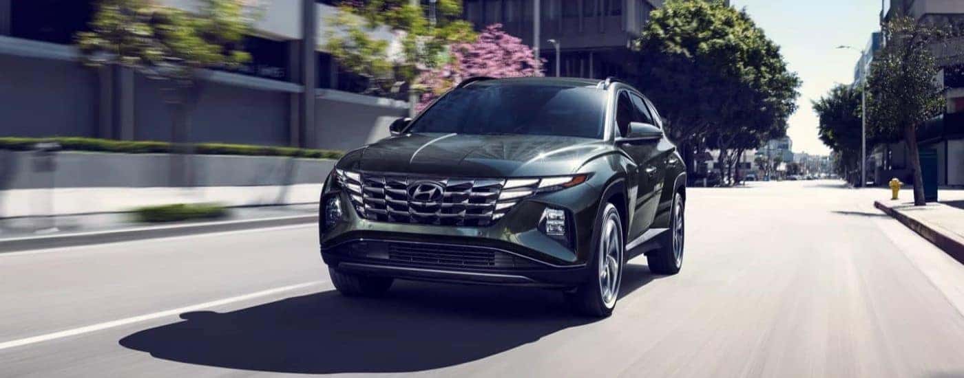A dark green used 2023 Hyundai Tucson Hybrid Limited driving down a city street