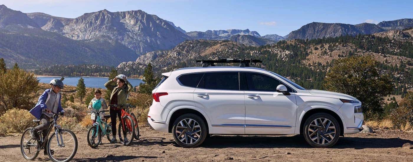 People riding bicycles near a white 2023 Hyundai Santa Fe for sale parked off-road.
