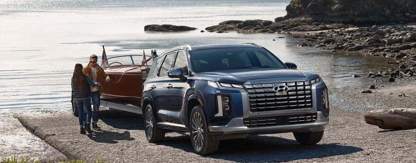 Blue 2024 Hyundai Palisade for sale towing a boat out of a lake.