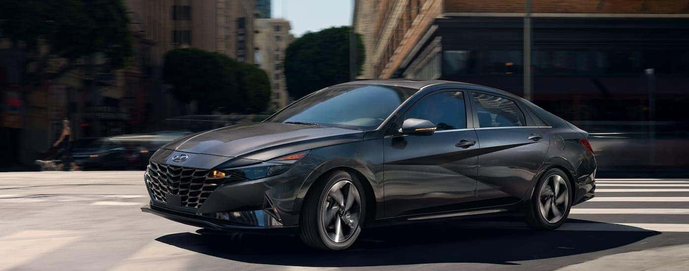 Black 2022 Hyundai Elantra driving through an intersection from a used car dealer.