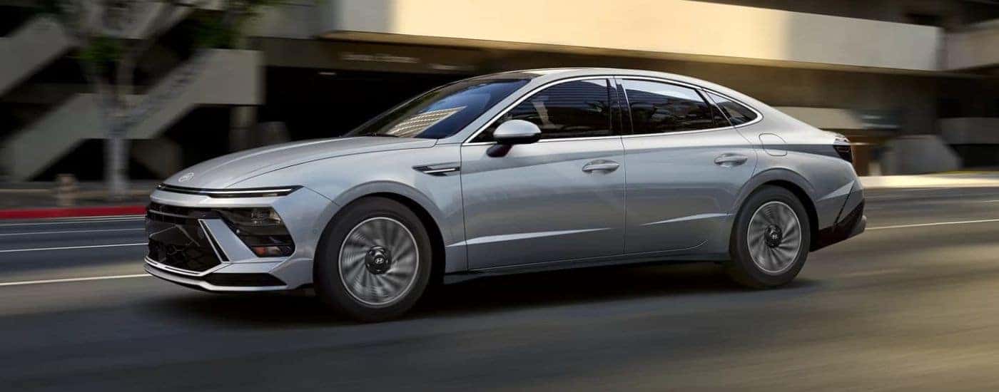 A silver 2024 Hyundai Sonata Hybrid Limited driving shown on driver side.