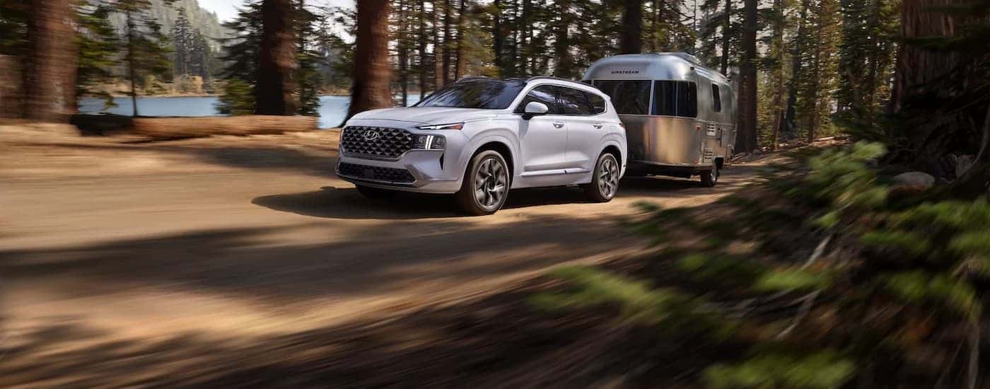 A white 2023 Hyundai Santa Fe towing a camper down a trail.