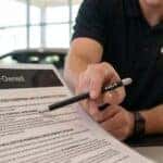A Kia dealership team member using a pen to point to the 10-year 100,000-mile powertrain limited warranty extension on a Kia Certified Pre-Owned document for a customer.
