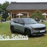A grey Kia Seltos X-Line parked on a lawn next to a freestanding Kia Seltos display sign.