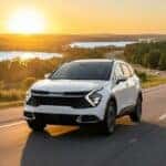 A modern white Kia Sportage SUV driving on a scenic highway with the signature rolling hills and green cypress trees of Clermont, Florida at sunset.