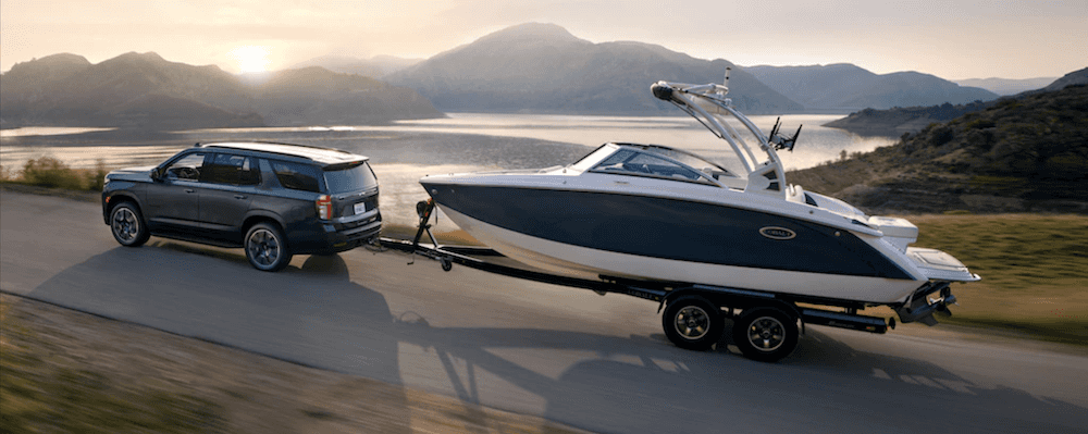 2021 chevy tahoe black exterior towing boat behind it on road with water in the backdrop