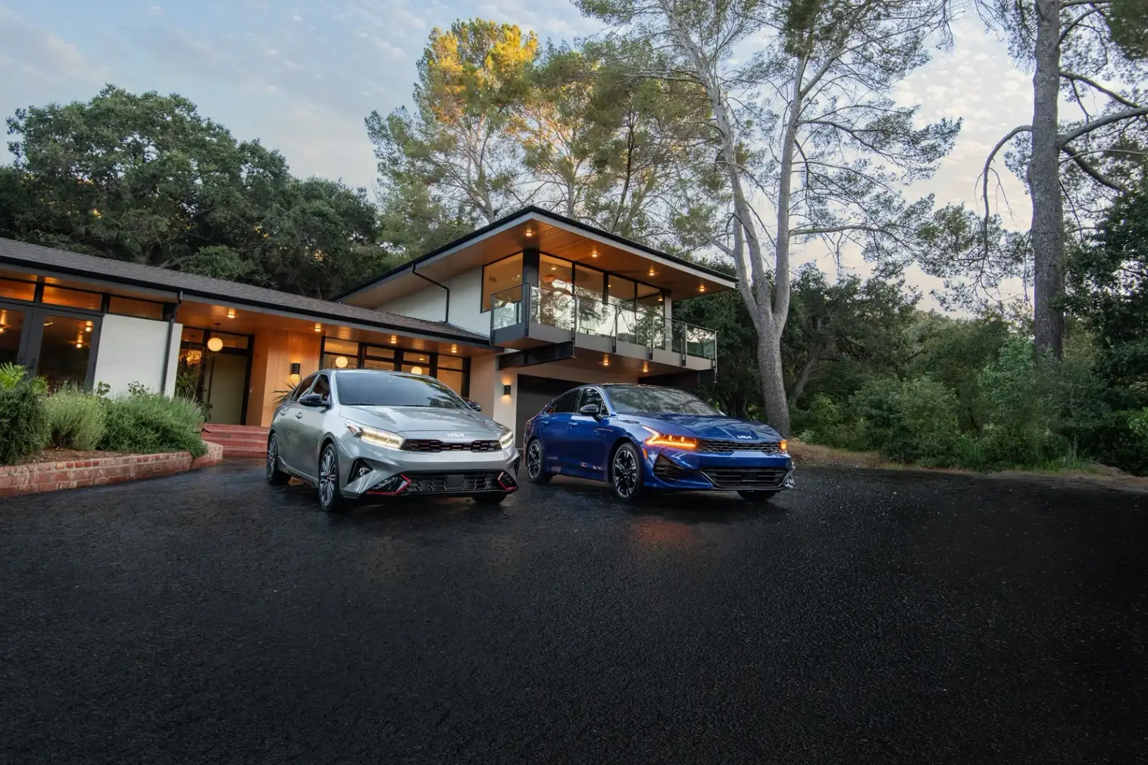 A silver Kia K5 and blue Kia K5 parked on a driveway