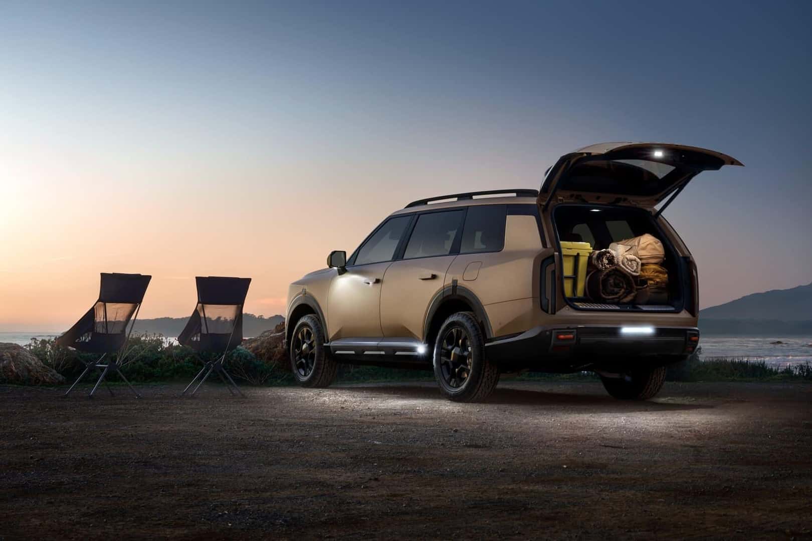 Kia Telluride on beach at sunset with two chairs beside it