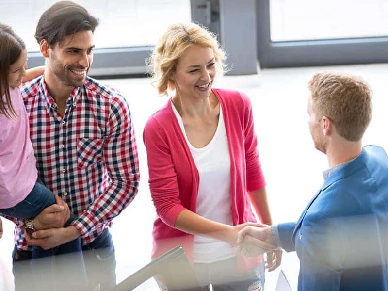 John Amato Finance Center A woman and her family shaking hands with a car dealer at a dealership