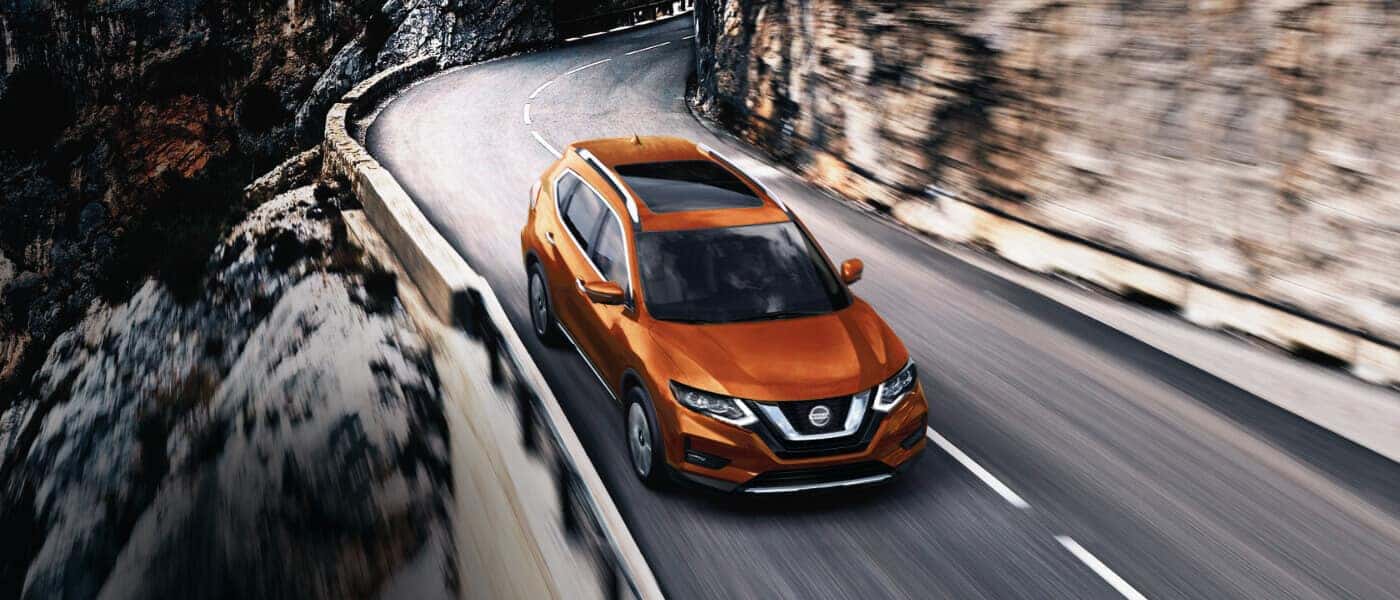 2020 Nissan Rogue An orange 2020 Nissan Rogue driving on a mountain road