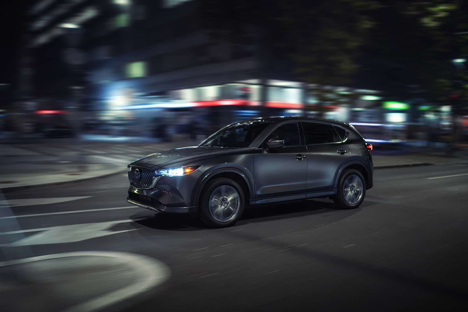 Silver 2025 Mazda CX-5 driving down a city road at night.