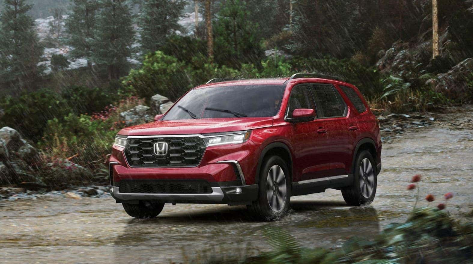Red 2023 Honda Pilot SUV while raining in front of forest and mountain like setting