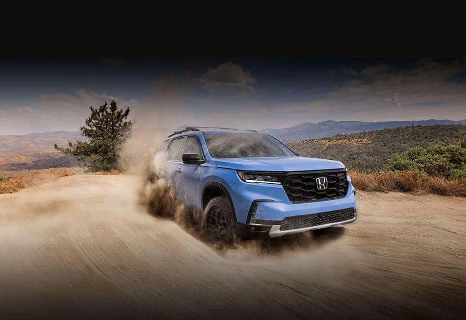 2025 Honda Pilot driving on sandy dune road with mountains in background