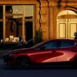 A red 2020 Mazda3 Hatchback in the golden hour against a building.