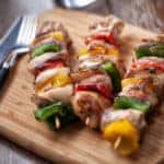 Three chicken kebabs on a wooden cutting board with a knife and fork.