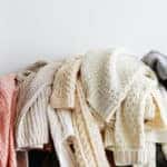 Bunch of sweaters of different material and knitting pattern in pile on gray sofa.