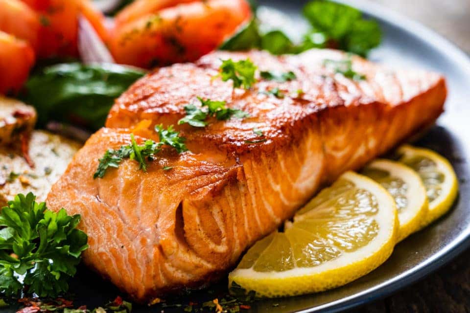 Grilled salmon on a plate with lemon slices and green garnish