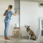 Woman painting a living room wall with a dog at her side