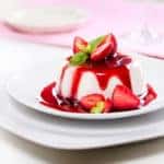 Close up photograph of panna cotta with strawberries on two stacked white plates.