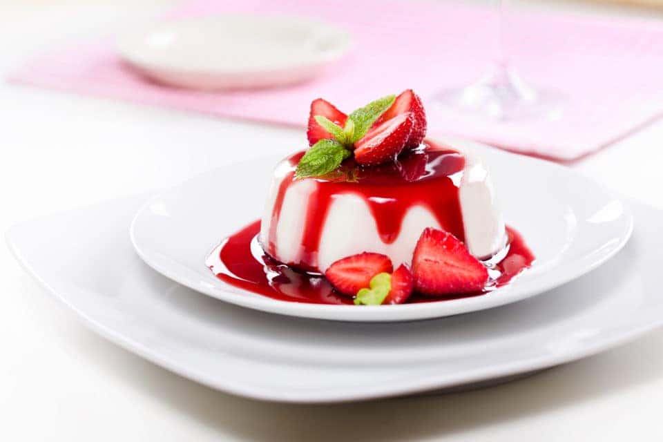 Close up photograph of panna cotta with strawberries on two stacked white plates.
