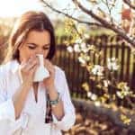 young adult woman coughing and sneezing outdoors with allergies