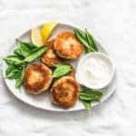 overhead view of salmon patties on white table with greens and white sauce