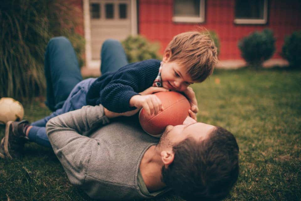 Photo of little smiling boy and his dad, playing American football in their backyard