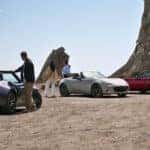 Three individuals pose beside their sleek Mazda Miata sports cars, showcasing their sleek and beautiful design.