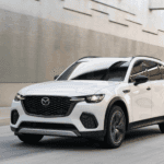 A 2025 Mazda CX-70 PHEV drives along a bustling city street, showcasing its sleek design and urban versatility.