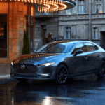 A 2025 Mazda3 sedan parked in front of a modern building, showcasing its sleek design against an urban backdrop.