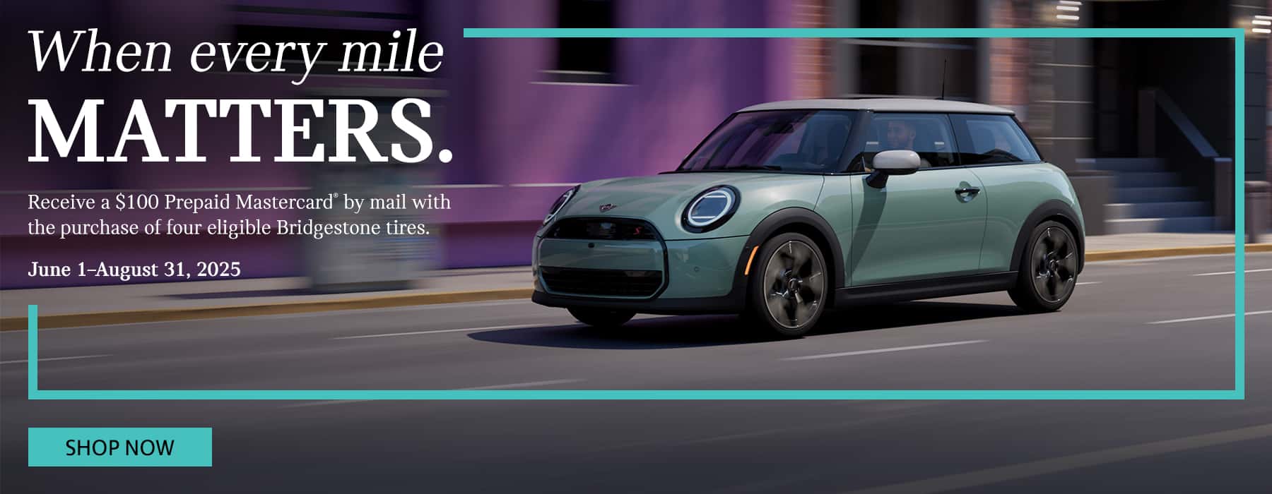 A green MINI 2-Door Hardtop drives down a city street passing pink buildings.