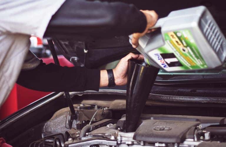 mechanic pouring oil into funnel on engine