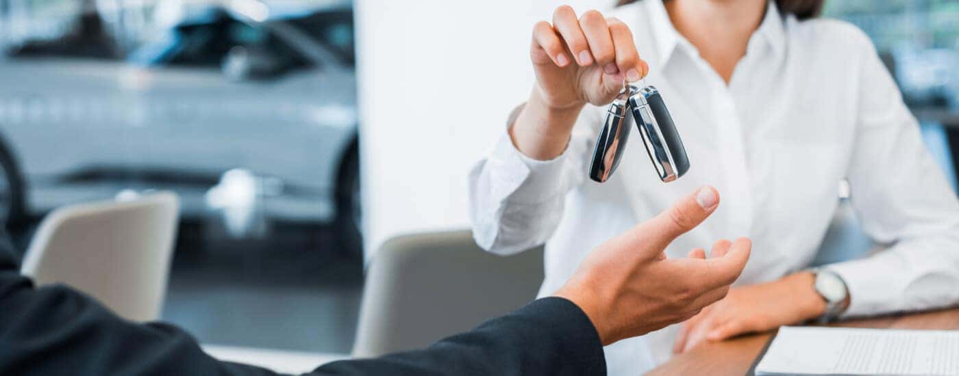 Cropped view of happy car dealer giving car key to man