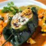 stuffed poblano pepper on a plate of sauce