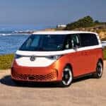 2025 ID. Buzz with Candy White over Energetic Orange paint, parked in front of a vast ocean background.