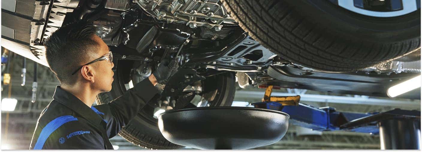 Volkswagen service technician performing an oil change under a vehicle on a lift.